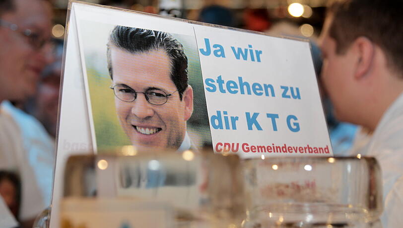 Ein Schild mit einem Foto des zurueckgetretenen Verteidigungsministers Karl-Theodor zu Guttenberg (CSU) und der Aufschrift "Ja wir stehen zu Dir K T G. CDU Gemeindeverband" steht am Mittwoch in Passau in der Dreilaenderhalle beim Politischen Aschermittwoch 2011 der CSU auf einem Biertisch. Ein Schild mit einem Foto des zurueckgetretenen Verteidigungsministers Karl-Theodor zu Guttenberg (CSU) und der Aufschrift "Ja wir stehen zu Dir K T G. CDU Gemeindeverband" steht am Mittwoch in Passau in der Dreilaenderhalle beim Politischen Aschermittwoch 2011 der CSU auf einem Biertisch.