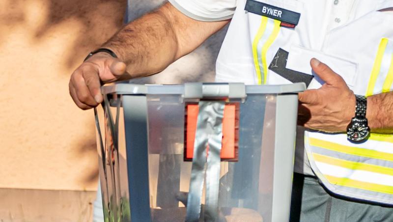 Ein Reptilienexperte trägt die eingefangene Monokelkobra in einem Behälter aus einem Hauseingang. Ein Reptilienexperte trägt die eingefangene Monokelkobra in einem Behälter aus einem Hauseingang.