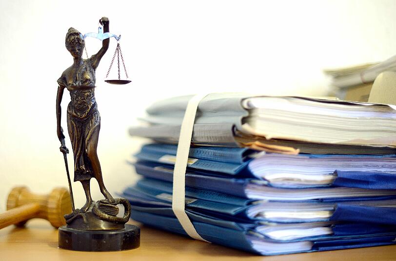 Eine Figur der Justitia, der altrömischen Göttin der Gerechtigkeit, neben einem Stapel Gerichtsakten. (Symbolbild)
