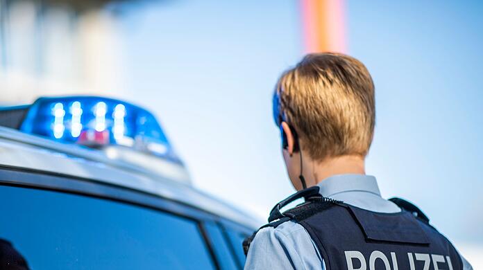 Eine Polizistin steht vor einem Streifenwagen.