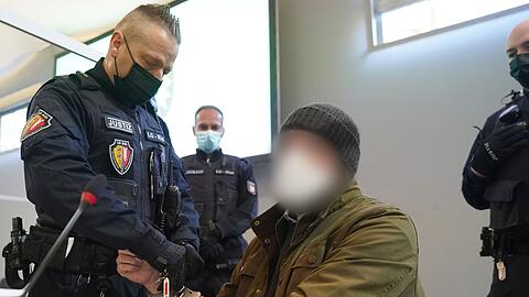 Ein Justizbeamter entfernt die Handschellen des Angeklagten (2.v.r) im Sitzungssaal des Landgerichts Kiel.