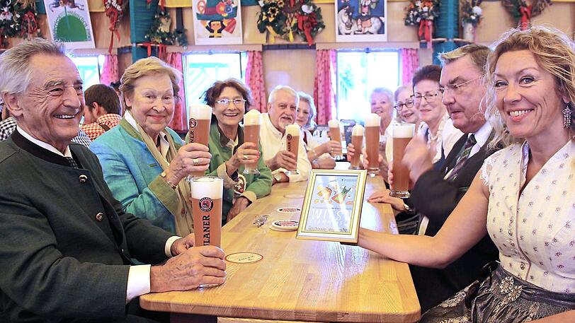 Am Seniorentisch geht es gemütlich zu. Die Pressesprecherin der Kleinen Wiesnzelte, Sabine Barthelmeß, zeigt das Wiesn-Stammtisch-Schild.