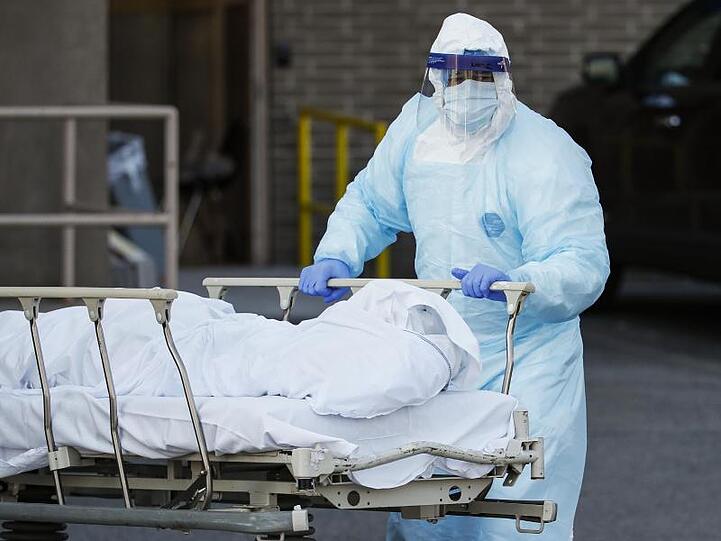 Ein Mitarbeiter in Schutzkleidung bringt eine Leiche zu einem Kühlanhänger, der als behelfsmäßige Leichenhalle im Wyckoff Heights Medical Center in New York dient.