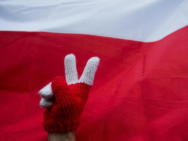 Peace-Zeichen vor polnischer Nationalflagge während eines Protests gegen die Justizreform. Polens Regierung hat die umstrittene Zwangspensionierungen oberster Richter zunächst wieder aufgehoben.