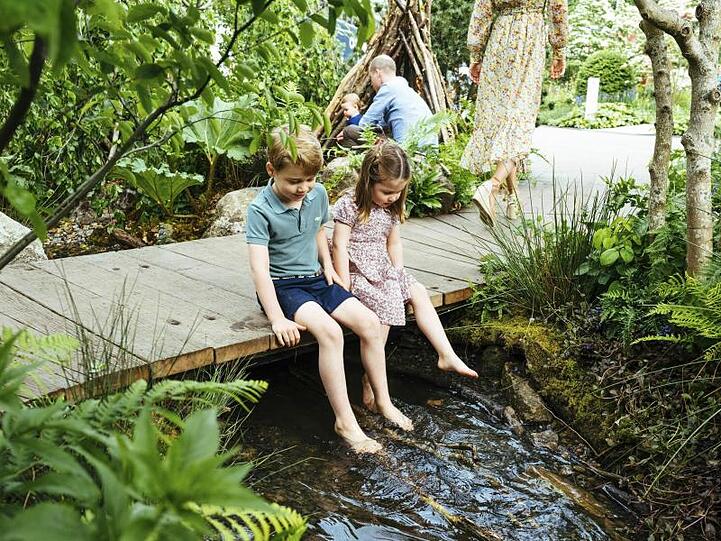 Der britische Prinz George und seine Schwester, Prinzessin Charlotte, lassen ihre Füße über einem Bach baumeln.