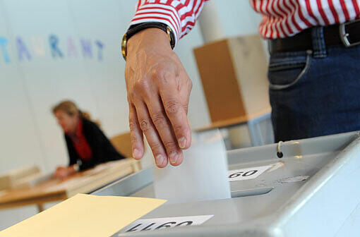 Ein Mann wirft am Sonntag in München einen Stimmzettel in eine Wahlurne.