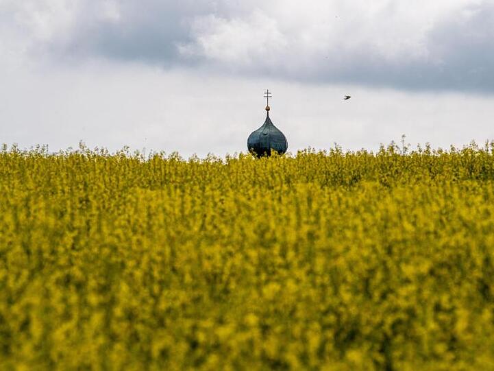 Die Kirchturmspitze von Rudlfing in Bayern ragt über einem Rapsfeld auf. In den nächsten Tagen regnet es in wechselnden Regionen verbreitet.