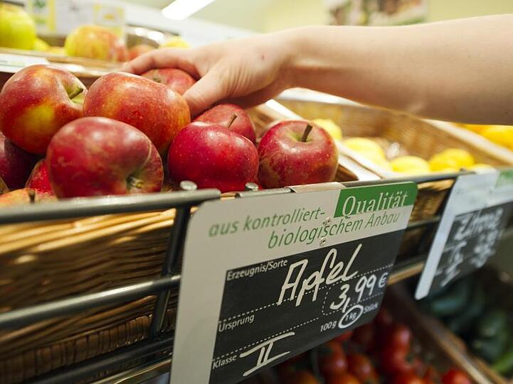 Eine Frau greift nach einem Apfel aus dem Obst- und Gemüseregal eines Reformhauses.