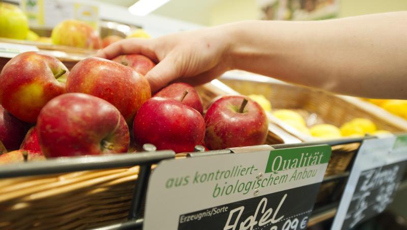 Eine Frau greift nach einem Apfel aus dem Obst- und Gemüseregal eines Reformhauses.