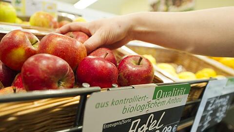 Eine Frau greift nach einem Apfel aus dem Obst- und Gemüseregal eines Reformhauses.