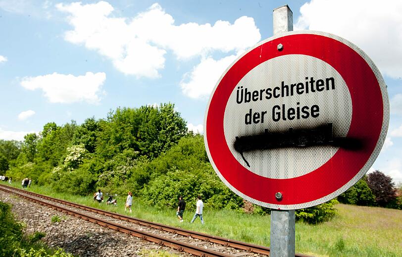 Jugendliche gehen am Samstag zu einer Brücke der Autobahn A7 bei Memmingen an einem Schild mit der Aufschrift "Überschreiten der Gleise verboten" vorbei. Jemand hat das Wort "verboten" mit schwarzer Farbe verdeckt.
