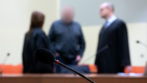 Der Angeklagte (M) steht vor Prozessbeginn mit seinen Anwälten Stephan Beukelmann (r) und Mariana Sacher im Gerichtssaal.