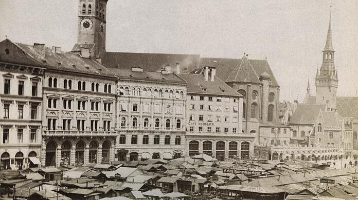 Kustermann (zweites Haus v.l.) gehörte schon 1895 zum Viktualienmarkt wie das Gemüse. Die Häuserreihe hat sich seitdem kaum verändert. Die Standl auf dem Markt schon.