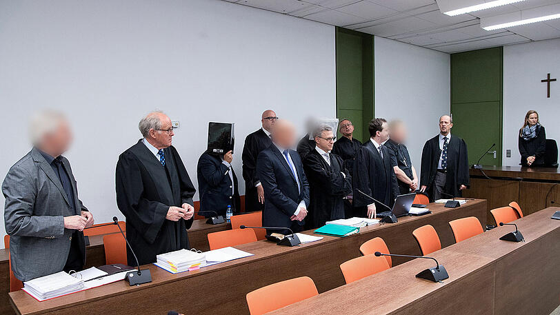 Millionenbetrug: Die fünf Angeklagten stehen vor Prozessbeginn mit ihren Anwälten im Verhandlungssaal des Landgerichts.