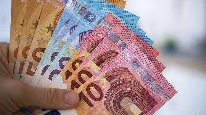 Eine Frau hält Banknoten von 10, 20 und 50 Euro gefächert in der Hand.