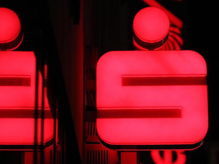Ein Sparkassenlogo spiegelt sich in einer Schaufensterscheibe. Foto: picture alliance/Karl-Josef Hildenbrand/dpa/Archivbild