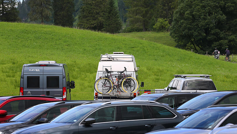 Bayern, Oberstdorf: Ausflügler fahren auf ihren Fahrrädern hinter dem gut gefüllten Parkplatz an der Talstation der Fellhornbahn.
