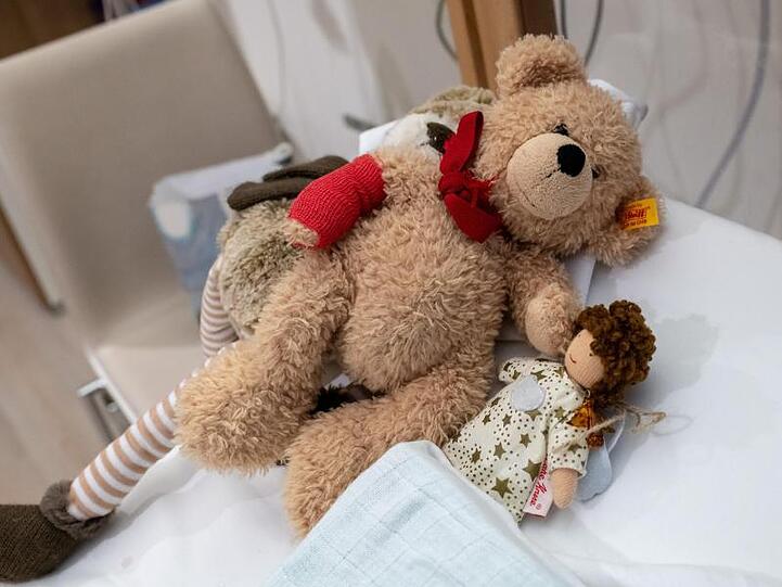 Puppen und Teddybären liegen auf einem Bett eines Patientenzimmer. Foto: Peter Kneffel/Archiv