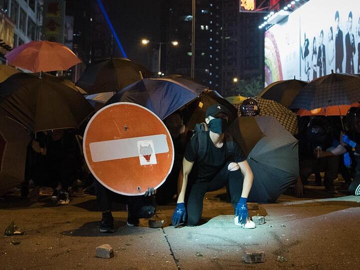 Demonstranten bilden hinter Regenschirmen gegen die Polizei eine Barrikade.
