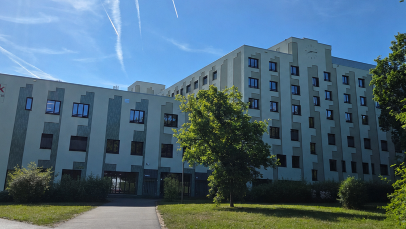 Der Haupteingang &uuml;ber den Sanatoriumsplatz an der Trambahnhaltestelle. Wegen des Klinik-Umzugs kommt es zu wichtigen &Auml;nderungen f&uuml;r Patientinnen und Patienten. (Transparenzhinweis: Auf dem Foto wurde mit KI ein Bauzaun entfernt.)