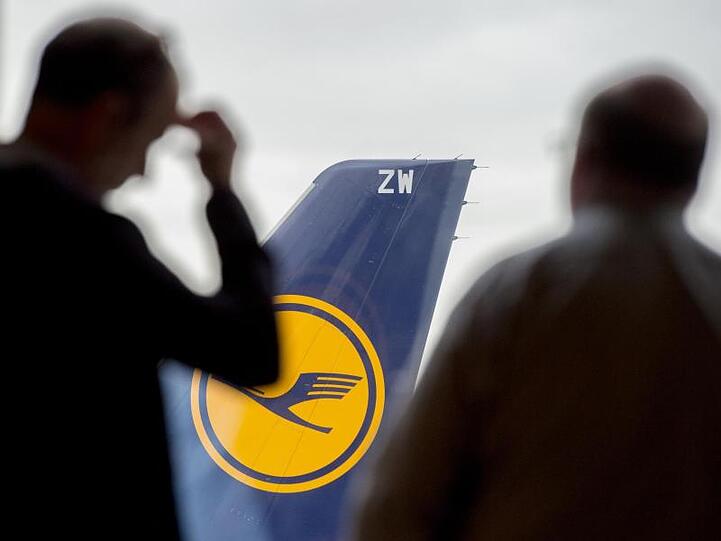 Zwei Männer blicken auf dem Flughafen durch ein Fenster auf eine abgestellte Lufthansa-Maschine. Foto: Boris Roessler/dpa/Archivbild