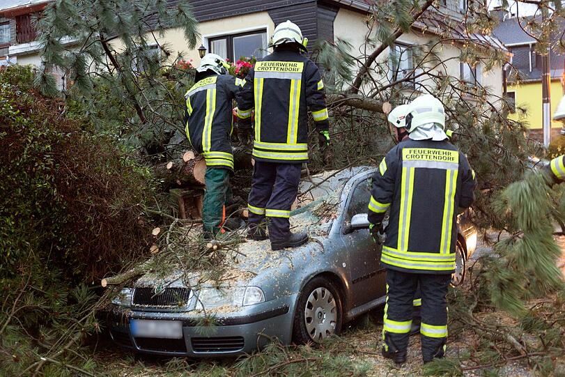 Crottendorf (Sachsen): Feuerwehrleute zersägen einen Baum, der auf ein Auto gestürzt ist.