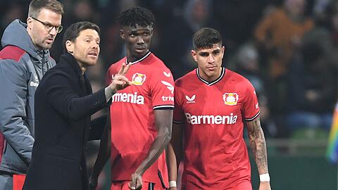 Leverkusens Trainer Xabi Alonso (l) spricht an der Seitenlinie mit Odilon Kossounou und Piero Hincapie (r).