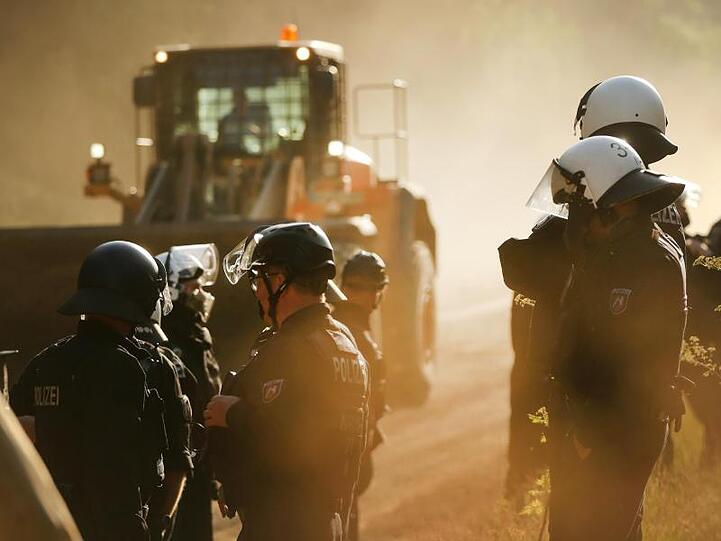 Polizisten stehen im Hambacher Forst neben einer Planierraupe.
