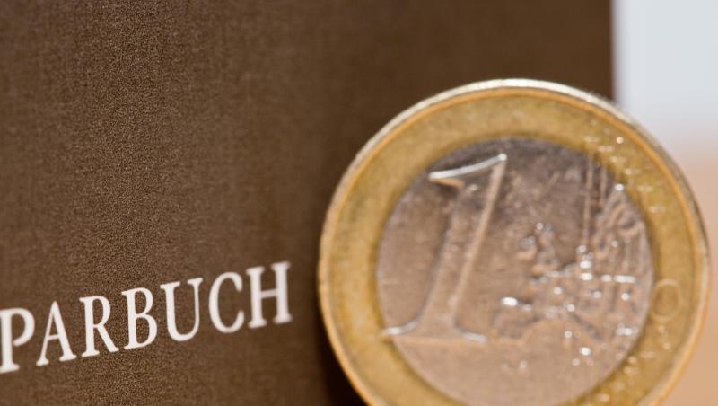 Eine Ein-Euro-Münze steht neben einem Sparbuch.