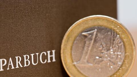 Eine Ein-Euro-Münze steht neben einem Sparbuch.