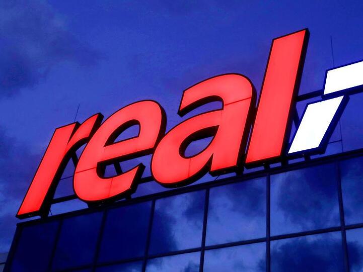 Das Real-Logo leuchtet am Morgen auf dem Dach eines Real Warenhauses in Köln.