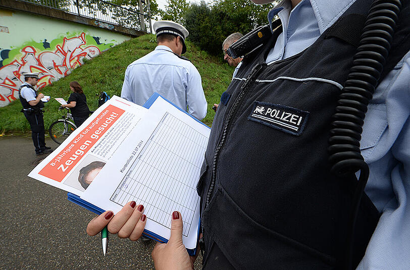 Eine Polizeibeamtin hält in Freiburg am Fundort ein Flugblatt mit einem Foto des getöten achtjährigen Armani in den Händen.