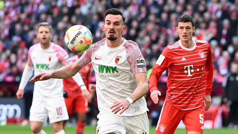 Benjamin Pavard (r) von München und Mergim Berisha von Augsburg kämpfen um den Ball.