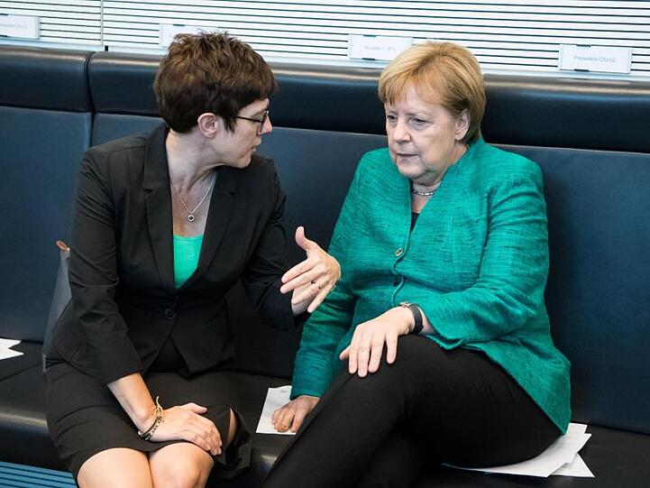 CDU-Generalsekretärin Kramp-Karrenbauer (l) und Kanzlerin Merkel unterhalten sich im Bundestag.