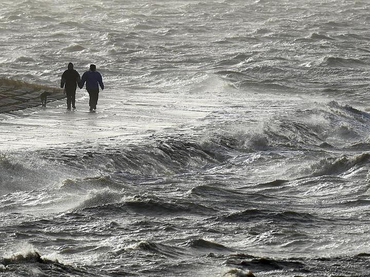 Passanten trotzen am Nordseedeich dem Sturm.