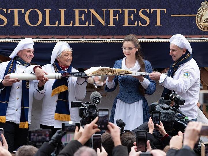 Das Dresdner Stollenmädchen und die Bäcker der Schutzgemeinschaft Dresdner Stollen präsentieren das erste Stück vom Riesenstollen.