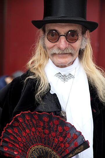 Ein Teilnehmer des Wave-Gotik-Treffens hat sich mit Zylinder, Fächer und runder Brille kostümiert.