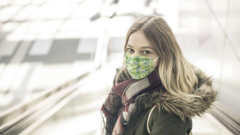 Eine junge Frau mit einem bunten &ndash; vermutlich selbstgebastelten &ndash; Mundschutz.