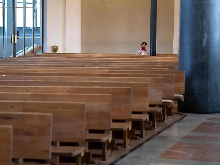 Eine Frau mit Mundschutz verfolgt einen Gottesdienst in einer Kirche. Foto: Sven Hoppe/dpa/Archivbild