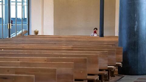 Eine Frau mit Mundschutz verfolgt einen Gottesdienst in einer Kirche. Foto: Sven Hoppe/dpa/Archivbild