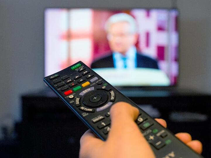 Eine Frau sitzt vor einem Fernseher und hält eine Fernbedienung in der Hand. Foto: Monika Skolimowska/Archivbild