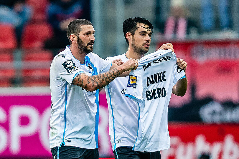 Ebenfalls ein denkwürdiger Moment: Im November 2019 verlässt Vereinslegende Daniel Bierofka, der mit den Löwen im Jahr nach dem Aufstieg den Klassenerhalt schaffte, den Klub. Beim ersten Spiel nach dem Abgang des Trainers in Halle bedankt sich unter anderem Mölders (hier mit Aaron Berzel) mit einer Trikot-Botschaft beim Ex-Coach.