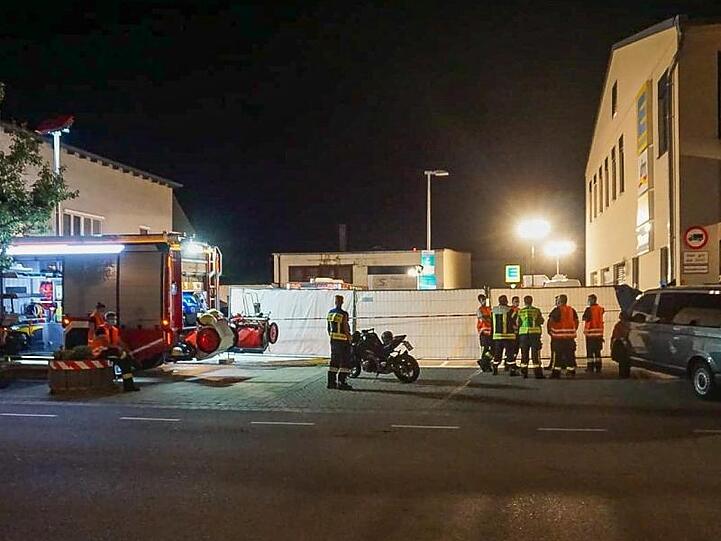 Feuerwehrleute stehen in der Nähe des Tatorts vor der Zufahrt zu einem Supermarkt. Foto: Markus Zechbauer/Zema Medien/dpa
