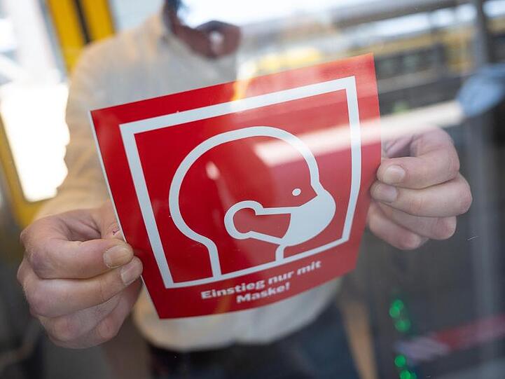 Ein Mann befestigt einen Hinweis zur Maskenpflicht in der Bahn. Foto: Sebastian Gollnow/dpa/Symbolbild