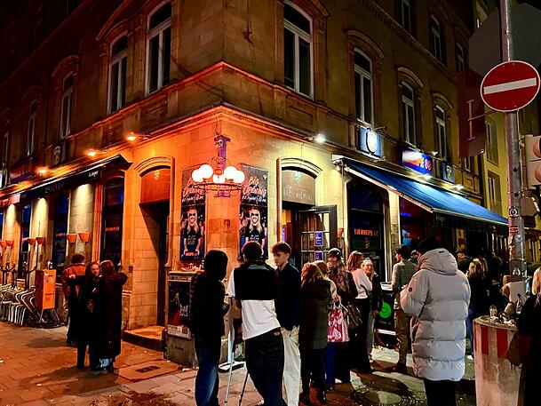 Vor der Kneipe 80 in der Theresienstra&szlig;e dr&auml;ngen sich am Abend junge Leute auf dem Gehweg &ndash; g&uuml;nstiges Bier und 80er-Jahre-Flair machen das Lokal zum beliebten Treffpunkt.