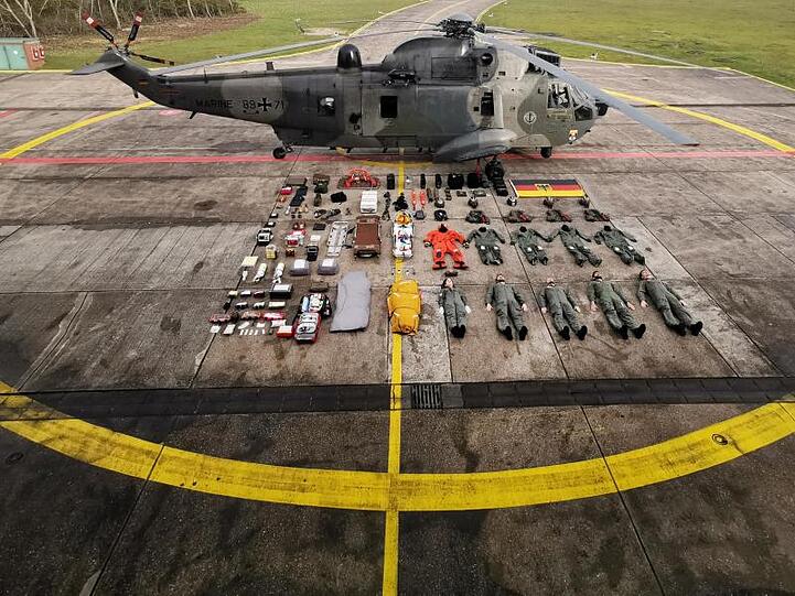 Fünf Seenotretter samt Ausrüstung liegen neben dem Rettungshelikopter SeaKing MK41.