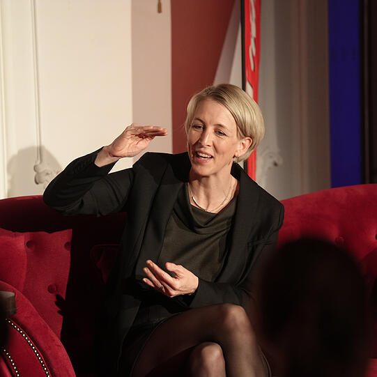 Adrian Prechtel im Gespräch mit Bürgermeisterin Katrin Habenschaden auf dem roten Sofa (von Möbel Höffner) in München.