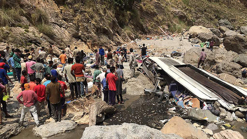 Helfer stehen in Chopal im indischen Bezirk Nerwa im Bundesstaat Himachal an der Unglücksstelle neben einem Bus, der zuvor in den Ausläufern des Himalaya-Gebirges von der Straße abgekommen war und hunderte Meter tief in den Fluss Tons gestürzt war.