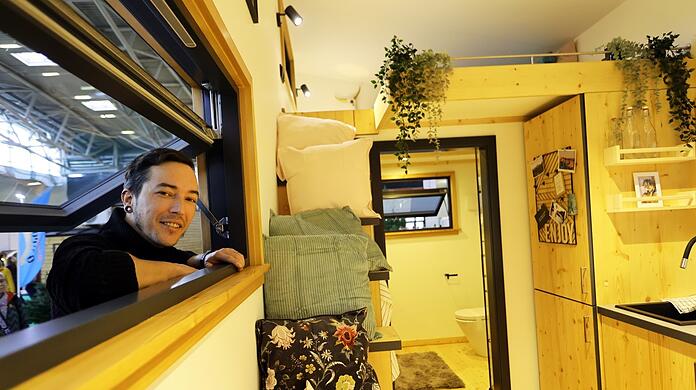 Markus Kastenberger schaut durch das Fenster des Tiny House des Herstellers "Winzig Wohnen" in der Messehalle B5. Der Holzexperte hat es selbst mitgebaut. Etwa 100.000 Euro würde das grundsätzlich mobile, 27 Quadratmeter große Häuschen samt Inneneinrichtung in etwa kosten. Es stecken rund 1.000 Arbeitsstunden drin.