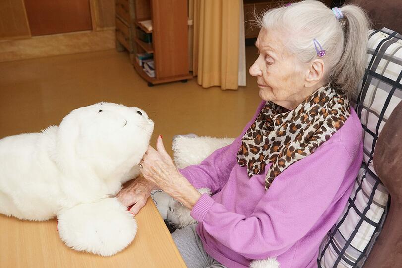 Erst als eine Roboter-Robbe vor ihr auf dem Tisch sitzt, werden die Gesichtszüge der Seniorin weicher.